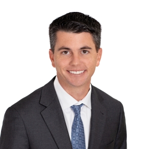 A smiling person wearing a suit and tie with a white background.