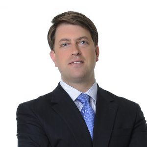 A person in professional attire with a blue tie and a confident expression.