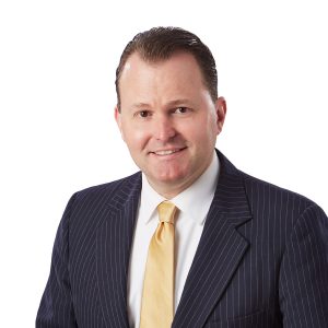 A man in a pinstripe suit with a yellow tie is posing for a professional portrait with a white background.
