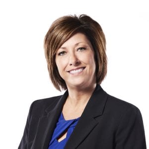 A professional portrait of a smiling woman with short hair wearing a black blazer and a blue blouse.