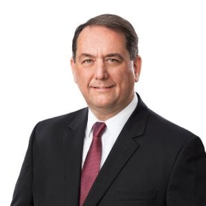 A person dressed in a professional black suit with a burgundy tie is posing against a white background.