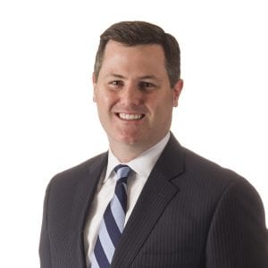 A smiling individual is dressed in a professional suit and tie against a white background.