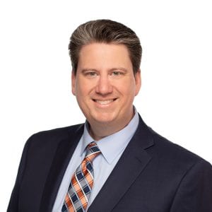 A smiling man in a blue suit with a striped tie is posing against a plain background.