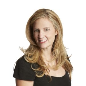 A smiling woman with long blonde hair wearing a black top poses against a white background.
