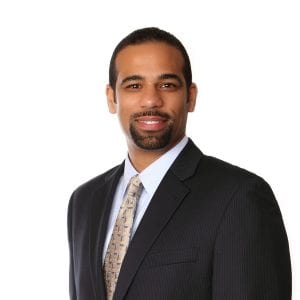 A smiling individual in professional attire against a plain background.