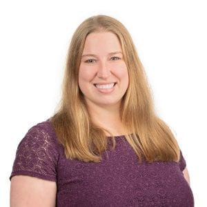 A person with long blond hair is smiling and wearing a purple shirt.