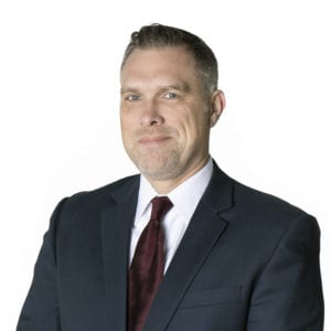A person wearing a suit and tie is posing against a plain white background.