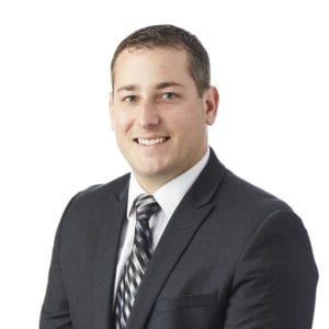 A man in a suit and tie smiles against a plain white background.