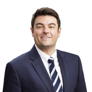 A man in a suit and striped tie is smiling against a white background.