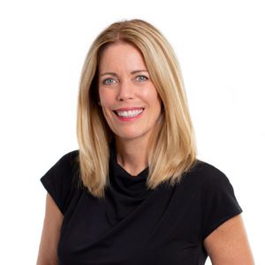 A smiling woman with straight blonde hair is wearing a black top against a white background.