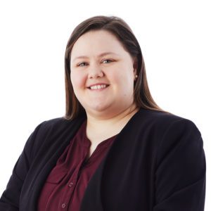 A person with long brown hair is smiling, wearing a dark blazer over a maroon blouse.