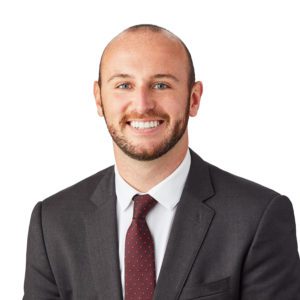A smiling man in a suit and tie stands against a white background.