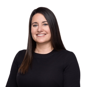 A person with long dark hair is smiling while wearing a black blazer and a gray shirt.