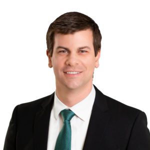 A person wearing a suit and a green tie, smiling with a white background.