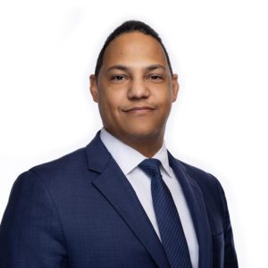 A person in a suit and tie is smiling against a plain white background.
