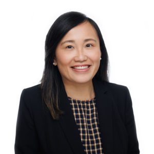 A woman with long dark hair and a black blazer smiles against a white background.