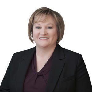 A person wearing a dark blazer and a maroon top smiles against a plain white background.