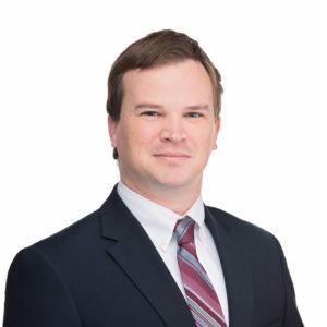 A man in a dark suit and striped tie is posing against a white background.