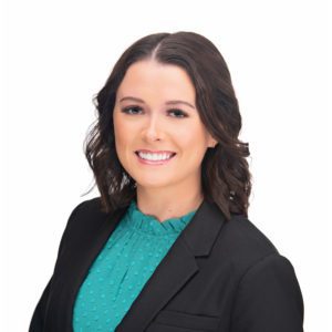 A woman with shoulder-length brown hair, wearing a teal blouse and a black blazer, smiles against a white background.