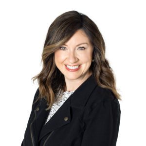 A smiling woman with wavy brown hair wearing a black blazer.