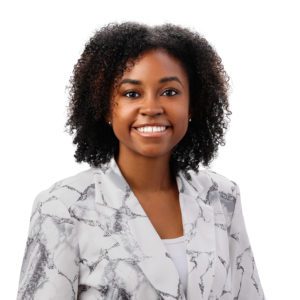 A person with curly hair is smiling and wearing a white top with a patterned blazer against a white background.