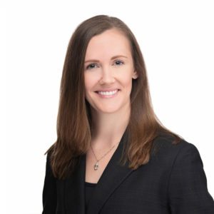 A woman with long brown hair is smiling while wearing a black blazer.