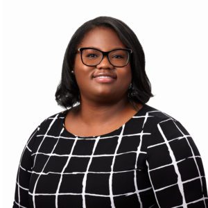A person with glasses wearing a black and white checkered top is smiling against a white background.