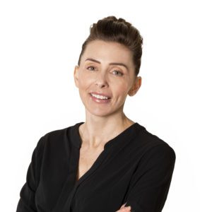 A person with short, styled brown hair is smiling while wearing a black shirt.