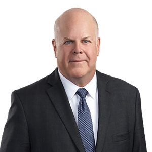 A bald man in a suit and tie poses against a plain white background.