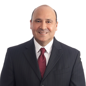 A person is smiling and wearing a dark suit with a red tie.