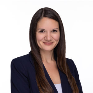 A person with long brown hair smiles while wearing a navy blazer.