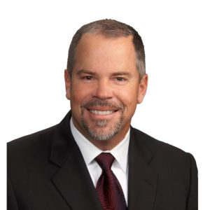 A man is smiling and wearing a suit with a red tie.