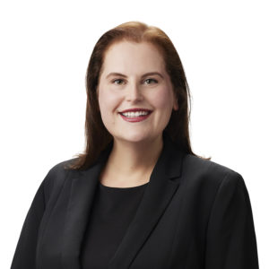 A person with long hair is wearing a black blazer and smiling against a white background.