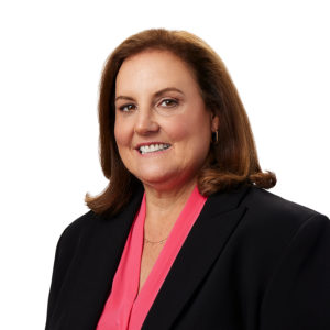A person wearing a pink blouse and black blazer smiles against a white background.