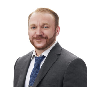 A man wearing a suit and tie smiles against a white background.