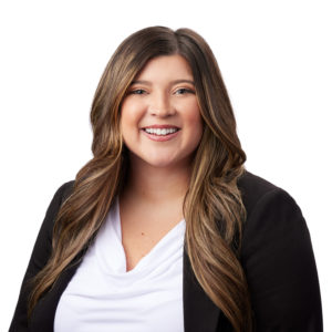 A smiling individual with long, wavy hair is wearing a white top and a black blazer.