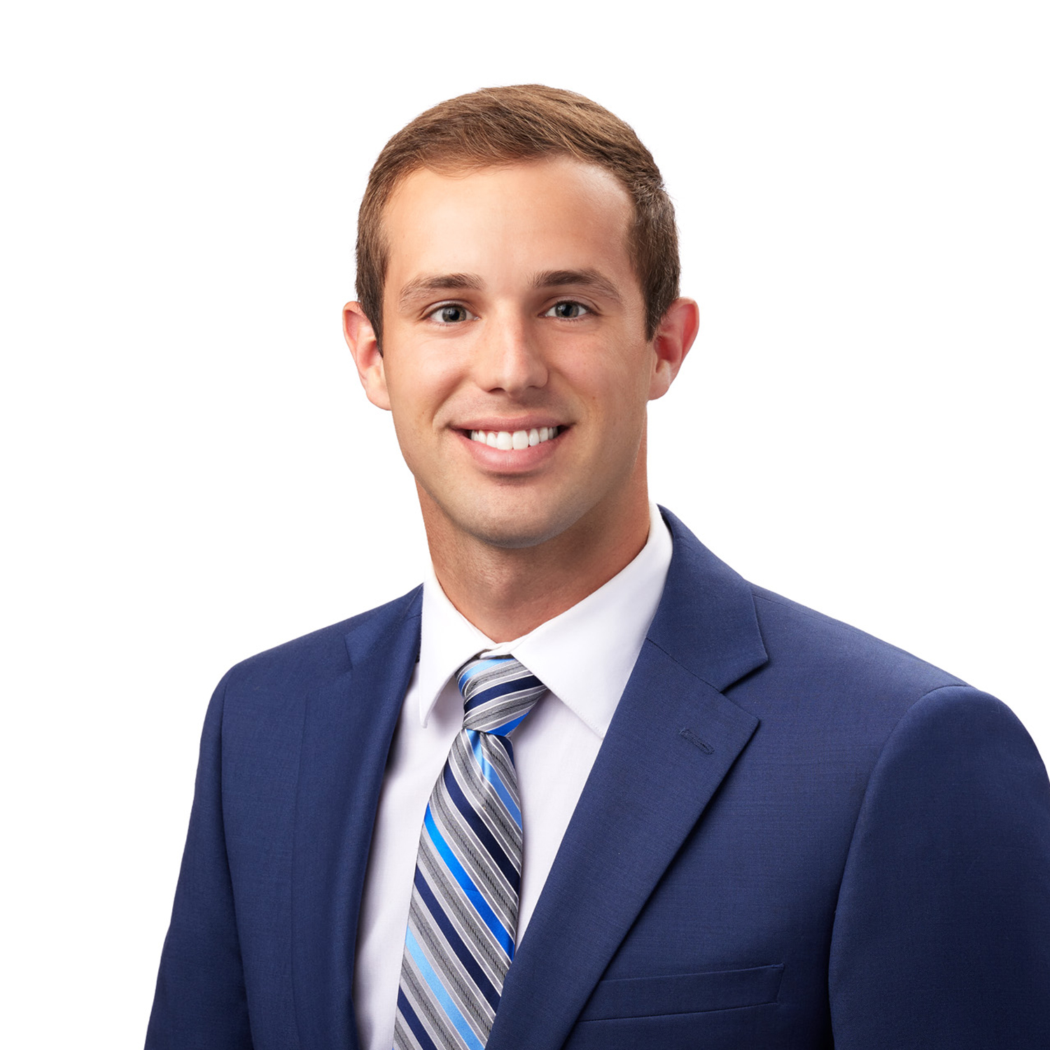 A person wearing a blue suit jacket, white shirt, and striped tie is smiling against a white background.