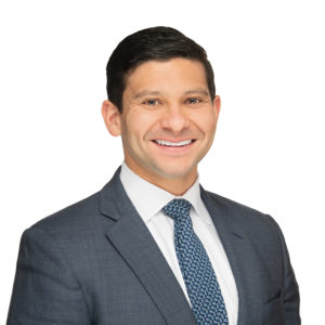 A person in a business suit is smiling against a plain white background.